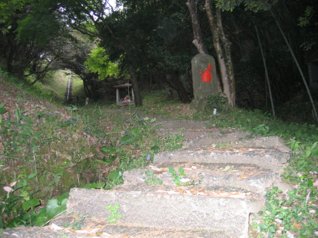 「高鍋八十八箇所霊場」の石段を登ったところ。霊場の入り口を示す大師像には「コノヤママワル　ダイシ」の言葉が刻まれている